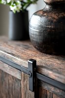 Rustic sliding barn door hardware detail with dark metallic vase on weathered wood surface, showcasing modern farmhouse interior design elements in soft natural lighting.
