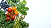 Fresh organic vegetables and fruits including cherry tomatoes, blueberries, spinach, kale, broccoli and asparagus arranged on white background for healthy eating.