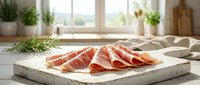 Sliced prosciutto ham arranged on wooden cutting board in bright kitchen setting for gourmet cooking and food preparation.