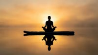 Silhouette of person meditating in lotus pose on wooden dock at golden sunset over calm water with reflection for wellness and mindfulness concepts.
