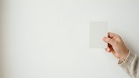 Young adult with medium skin tone holding blank white card against neutral background, suitable for business presentations, marketing campaigns, and promotional materials.