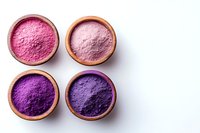 Vibrant pink and purple natural powder pigments in wooden bowls arranged on white background, top view composition for cosmetics and natural dye industry.