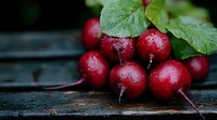 Fresh red radishes with water drops and green leaves on rustic wooden background, macro food photography with natural lighting and selective focus.
