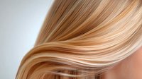 Smooth flowing blonde hair strands with honey and caramel highlights against light background, showing natural wave pattern and healthy shine. Professional salon result.