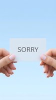 Female hands with pink nails holding a white card with the word Sorry on a soft blue background, conveying apology and reconciliation.
