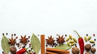 Aromatic spices and herbs arranged on white background with copy space. Cinnamon stick, star anise, bay leaves, chili peppers, cardamom pods for cooking.