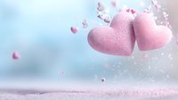 Pink textured hearts floating in dreamy pastel atmosphere with scattered small heart shapes and glitter particles against soft blue background.