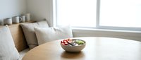 Fresh vegetable salad bowl on wooden table in bright modern living room with comfortable seating and natural light from large windows.