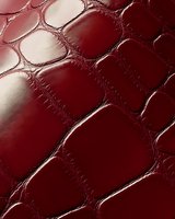 Burgundy red crocodile leather texture with glossy surface and distinctive scale pattern, showing natural reptilian skin structure and luxurious material detail.