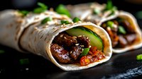 Mexican beef burritos with fresh cilantro and vegetables wrapped in flour tortillas on dark slate surface for restaurant menu and food photography.