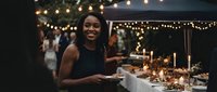 Young African American woman smiling at elegant outdoor dinner party with string lights and candles creating warm ambiance for celebration event.