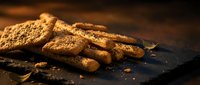 Crispy golden biscuits and breadsticks arranged on dark slate surface with warm lighting, suitable for food photography, bakery marketing, and culinary content.