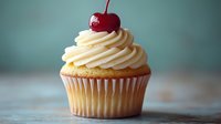Vanilla cupcake with swirled buttercream frosting topped with bright red maraschino cherry against blurred teal background, macro food photography.