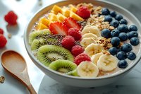 Colorful smoothie bowl topped with fresh kiwi, banana slices, raspberries, blueberries, chia seeds and granola on marble background. Healthy breakfast concept.