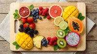 Colorful tropical and seasonal fruits arranged on wooden cutting board including mango, papaya, dragon fruit, grapefruit, berries and citrus for healthy eating.