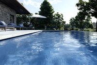 Luxurious infinity pool with blue rippling water against natural landscape, stone patio with loungers and umbrella, surrounded by lush green trees.