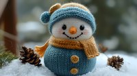 Adorable knitted snowman with blue hat and orange scarf sitting in snow with pine cones, winter holiday decoration for seasonal crafts and greeting cards.