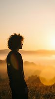 Young African American woman silhouette standing in golden sunset light over mountain landscape, contemplating nature and freedom during peaceful moment.