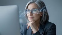 Professional mature businesswoman with gray hair wearing smart glasses with digital interface overlay in modern office environment for technology concepts.