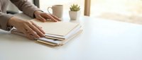 Professional woman organizing documents on clean white desk with coffee cup and succulent plant in bright modern office workspace.
