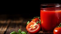 Fresh tomato juice in glass with ripe cut and whole tomatoes, green leaves on rustic wooden background. Natural healthy drink concept for detox.