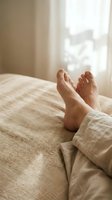 Bare feet resting on a linen bed with soft natural light, evoking morning relaxation, comfort, and a cozy lifestyle at home.