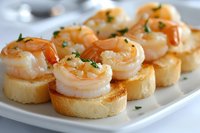 Succulent grilled shrimp appetizers served on toasted baguette rounds garnished with fresh herbs, arranged on white plate for elegant party catering or dining.