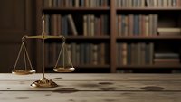 Golden scales of justice on wooden desk with blurred law library bookshelves in background for legal concepts and attorney office decor.