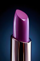 Pink metallic lipstick close-up on dark blue background, luxury cosmetic product photography with dramatic lighting and reflective surface detail.
