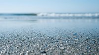 Wet sand beach with shallow waves and ocean horizon in soft focus, suitable for travel, nature, and coastal design projects.