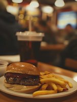 Juicy cheeseburger with melted cheese on brioche bun served with golden french fries on white plate in cozy restaurant setting with warm ambient lighting.