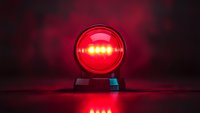 Glowing red emergency light beacon against dark background with dramatic reflection on surface, creating atmospheric warning ambiance.