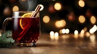 Steaming mulled wine with orange slice and cinnamon stick in glass mug against blurred holiday lights background, festive winter drink on wooden surface.