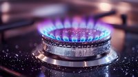 Blue flame gas burner with water droplets on dark surface, close up macro shot showing kitchen stove heat ring in action with natural gas combustion.