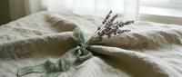 Dried lavender bouquet tied with sage green ribbon on natural linen bedding creates peaceful bedroom decor for relaxation and aromatherapy wellness.