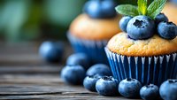 Fresh blueberry muffin topped with ripe berries and mint leaves on rustic wooden background, selective focus with natural lighting for food photography.