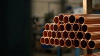 Stack of shiny copper pipes in industrial warehouse setting with warm lighting highlighting metallic surface texture for construction projects.