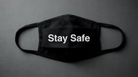 Black fabric face mask with Stay Safe text on dark background, symbolizing health protection and pandemic safety awareness.