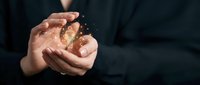 Professional businessman in dark suit holding glowing golden Bitcoin cryptocurrency coin in cupped hands against black background for investment concepts.