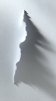Dramatic torn paper edge casting deep shadow on white surface creates abstract minimalist composition with strong contrast and textural detail.