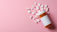 White prescription pills spilling from orange medication bottle on soft pink background for healthcare and pharmaceutical concepts.