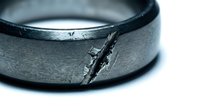 Cracked metal ring showing wear and damage with visible fracture line on silver band surface against white background for repair concepts.