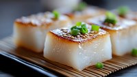 Seared scallops with caramelized golden-brown crust and fresh green garnish served on bamboo mat, close up view showing delicate texture and professional plating.