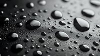 Water drops of various sizes on dark hydrophobic surface creating abstract pattern with light reflection. Macro photography showing surface tension.