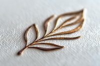 Elegant golden leaf branch embossed on white textured paper surface creates subtle shadow and depth effect, showcasing minimalist artistic design and craftsmanship.
