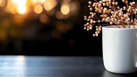 White ceramic vase with dried flowers on dark wooden table against blurred golden bokeh background creates cozy atmospheric mood for home decor and lifestyle design.