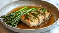 Pan seared salmon fillet with fresh asparagus spears and dill garnish in brown butter sauce served on rustic ceramic plate, close up view of gourmet meal.