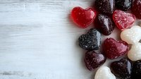 Colorful heart-shaped gummy candies arranged on rustic white wooden background, perfect for Valentine's Day or romantic food concepts.