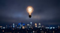 Glowing vintage light bulb floating above blurred city skyline at night. Creative innovation and bright ideas concept for business presentations and marketing.