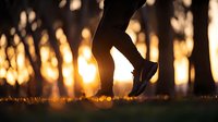 Silhouette of person jogging at sunset in park with golden bokeh lights through trees creating magical atmosphere. Active lifestyle and nature concept.